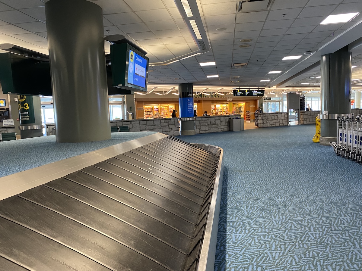 The luggage carousel at YVR domestic arrivals in the foreground, looking towards the low stone wall that separates the area from the rest of the airport.