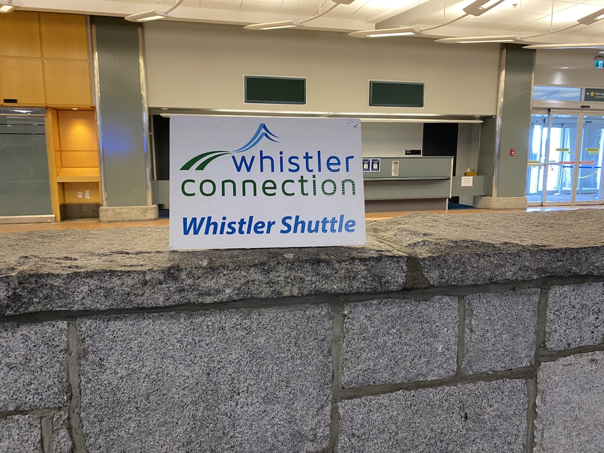 A Whistler Connection sign, resting on the short stone wall at YVR domestic arrivals.